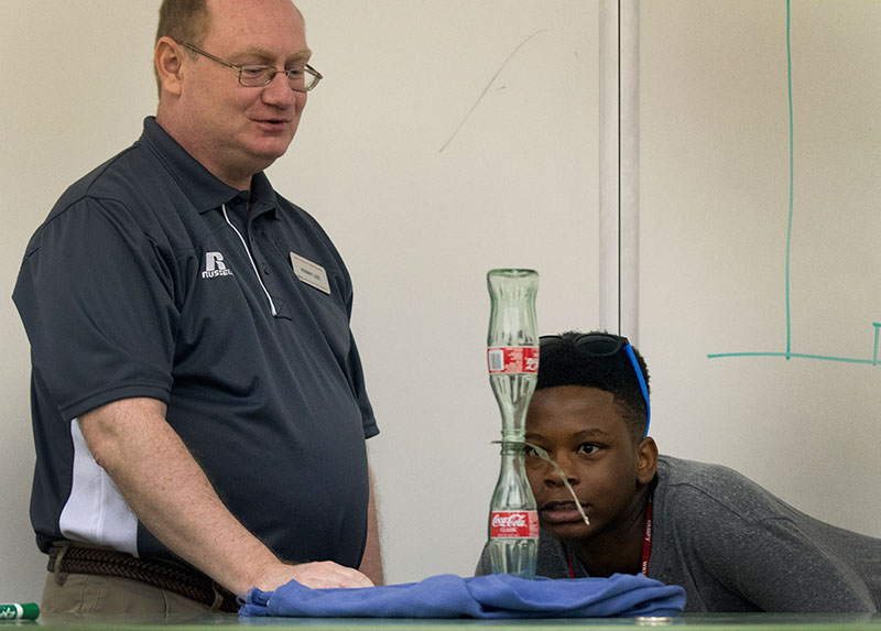 Ni'Kerrion McDonald of Lexington formulates a plan to pull a dollar bill out from between two Coca Cola bottle without making the top bottle fall while Physics teacher Kenny Lee waits to catch the bottle Wednesday, June 24. The task was meant to demonstrate Newton's first law of motion. (Photo by Sam Oldenburg)