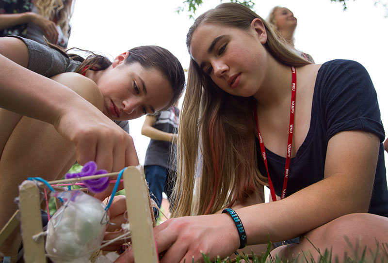 Karen Snyder (left) of Columbus, Ohio, and Laina Caywood of Georgetown make last-minute adjustments to their egg drop container before dropping it from the top of Parking Structure 2 Tuesday, June 23, during Problems You Have Never Solved Before.  (Photo by Sam Oldenburg)