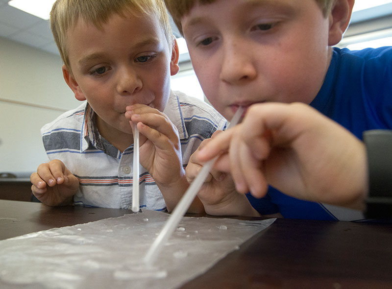 Jackson (left) and Max race to blow water droplets across wax paper in Science Monday, July 6, during Camp Explore. (Photo by Sam Oldenburg)