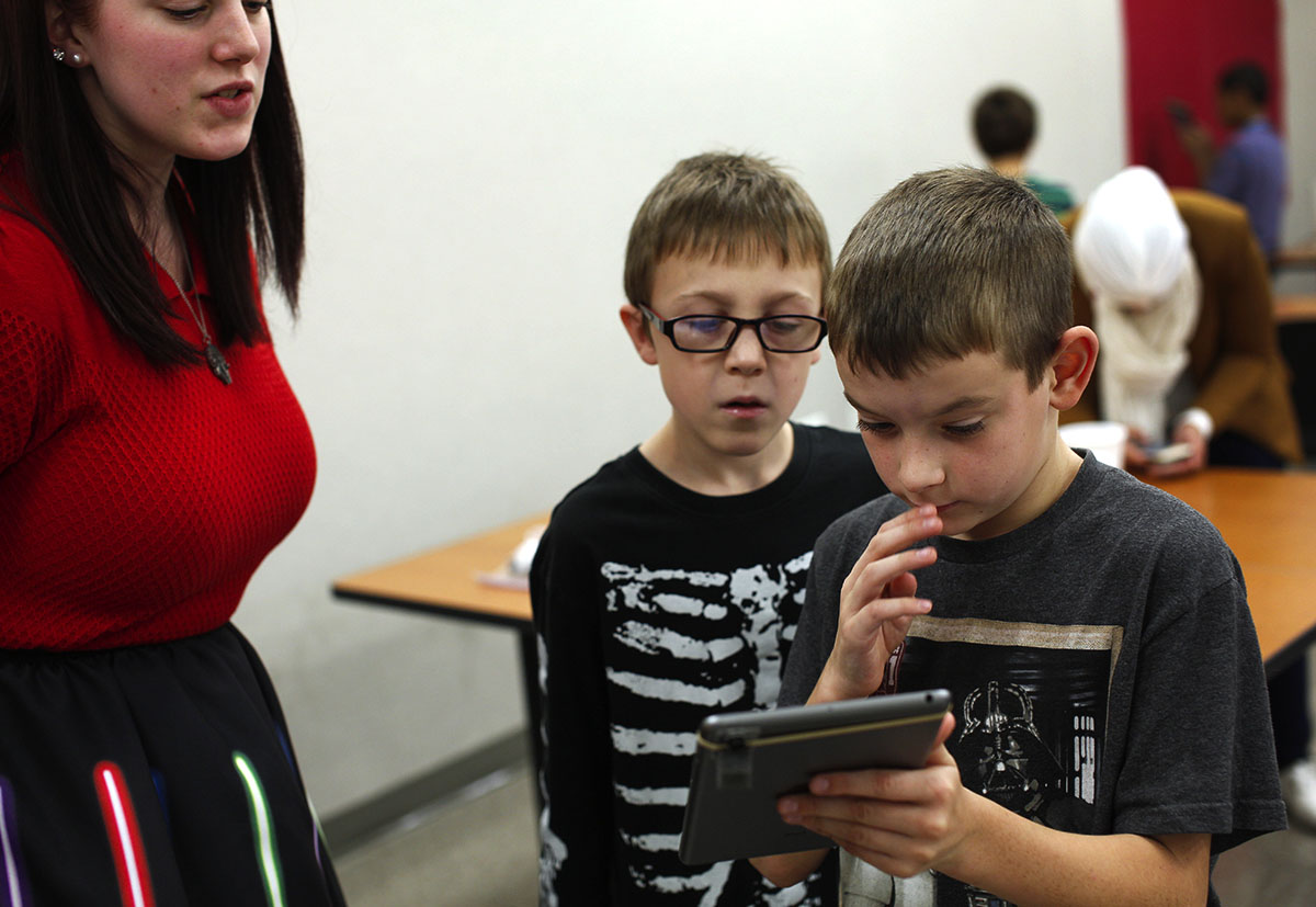 Bobby Morin (middle), 8, of Bowling Green, looks over his partner's shoulder to try and figure out if the photo they took matches one of the photos on the big screen in front of the class with the help of one of their teachers, Robin Tyler, in iPad iExplorations on Saturday, October 31. (Photo by Emilie Milcarek)