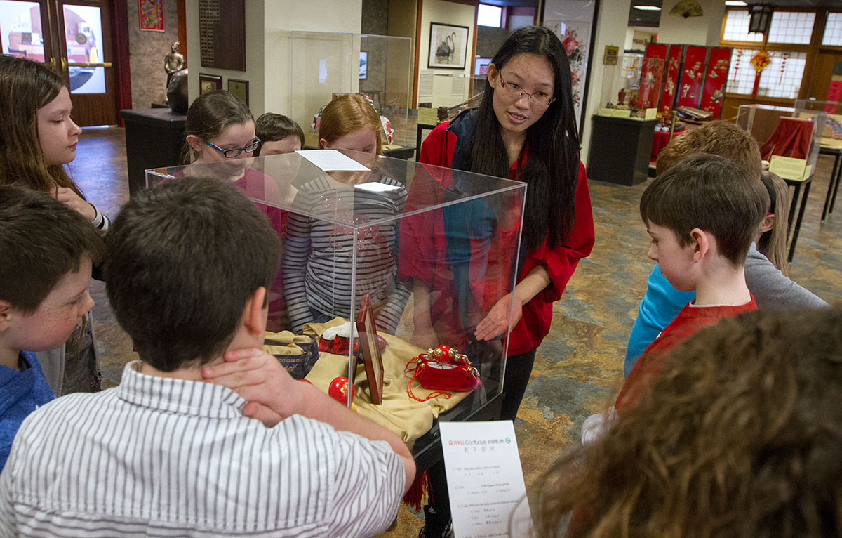 Create Your Own Chinese Masterpiece teacher Gu Fang talks about a display of emroidered shoes while leading her class on a tour of the Chinese Learning Center presented by the Confucius Institute in Helm Library.