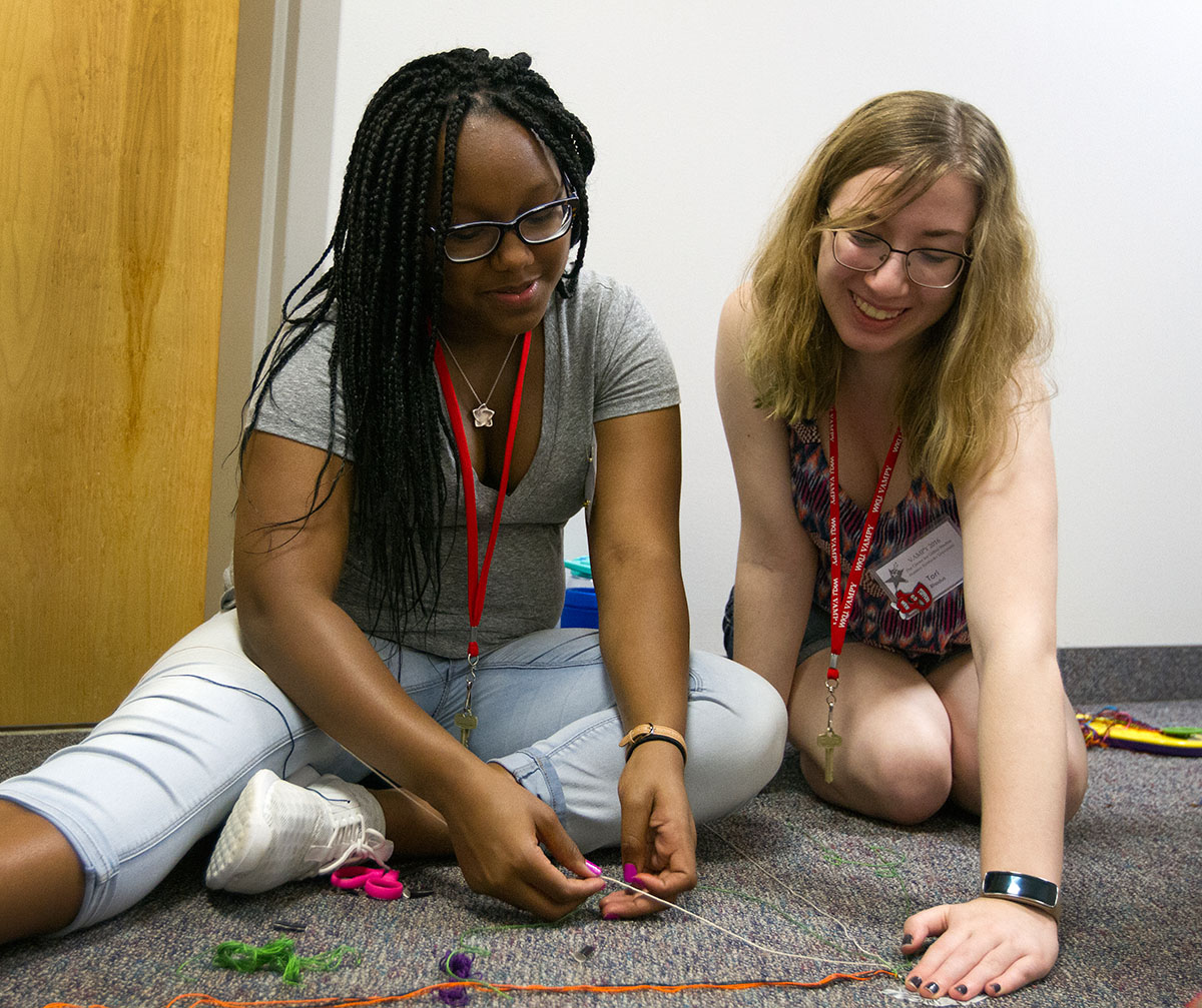 To'Nia Beavers (left) of Bowling Green makes a friendship bracelet with help from Tori Rhodus of Louisville during hall time Monday, June 27. During hall time, campers spend time with their hallmates in the same counselor group in the halls outside their rooms before going into their rooms for the night. (Photo by Sam Oldenburg)