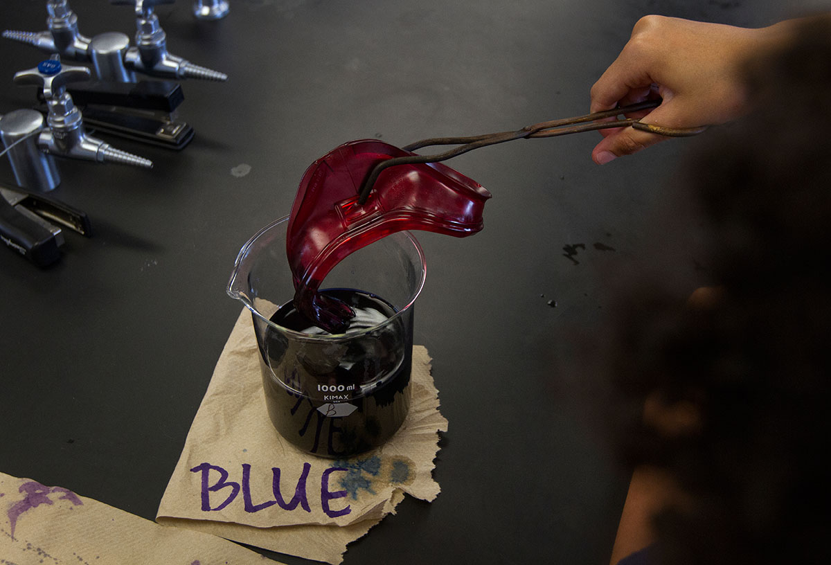 Sadibou Ceesay of Berea dips his goggles in blue dye during Chemistry of Everyday Monday, June 13. The students rinsed the goggles in cold water between dipping them in various colors to hold the color. (Photo by Sam Oldenburg)