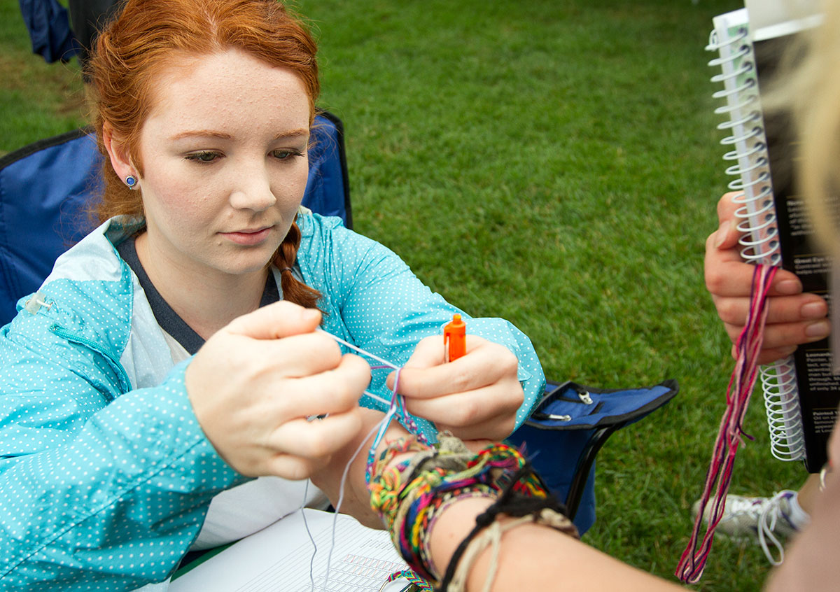 Counselor Courtney George ties a friendship bracelet on the wrist of one of her campers, Gracie Hobbs of Owensboro, after checking her in outside Northeast Hall at the end of classes Monday, June 27. (Photo by Sam Oldenburg)