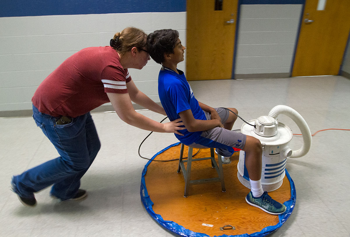 Physics teaching assistant Allison Gregory pushes Ronit Patel down a hallway on a hovercraft during a class trip to Warren Central High School Wednesday, July 13. (Photo by Sam Oldenburg)