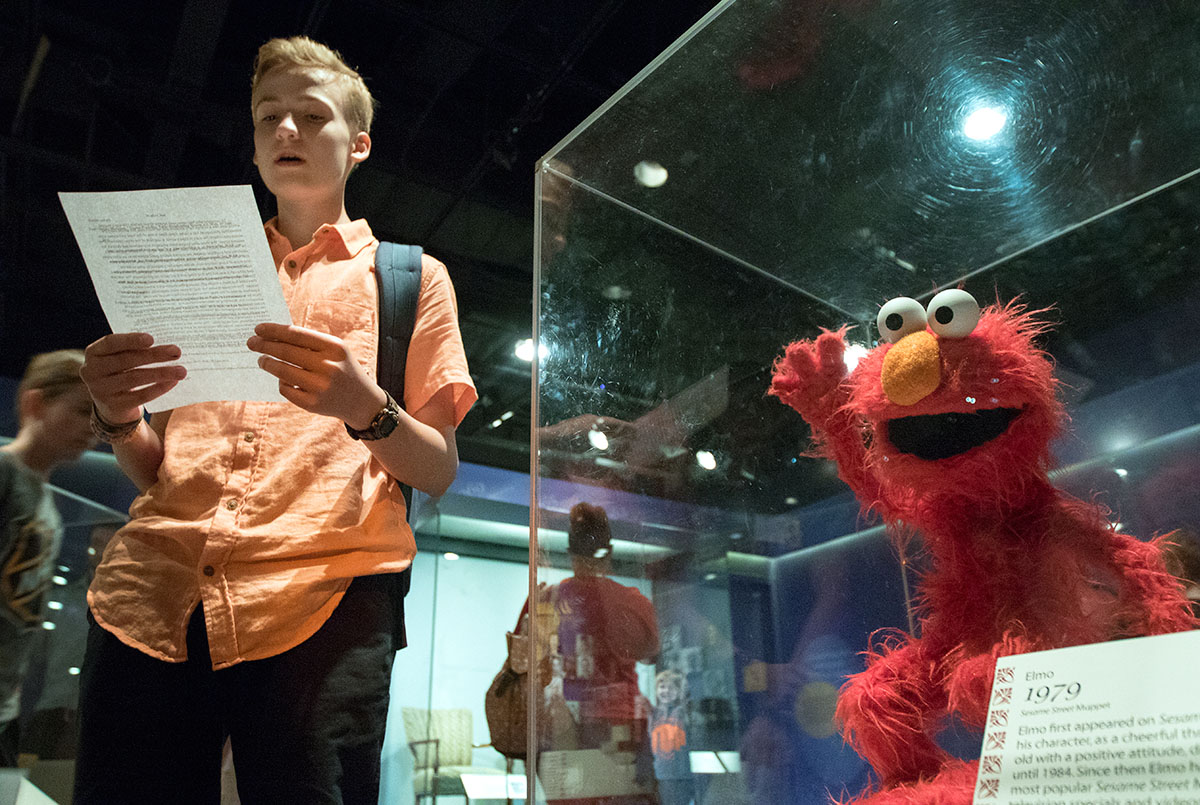Parker Woods of Brentwood, Tenn., reads his report on Elmo from "Sesame Street" beside the puppet in the American Stories exhibit at the Smithsonian National Museum of American History while on a field trip to Washington D.C. with the Pop Culture class Wednesday, July 6. (Photo by Sam Oldenburg)