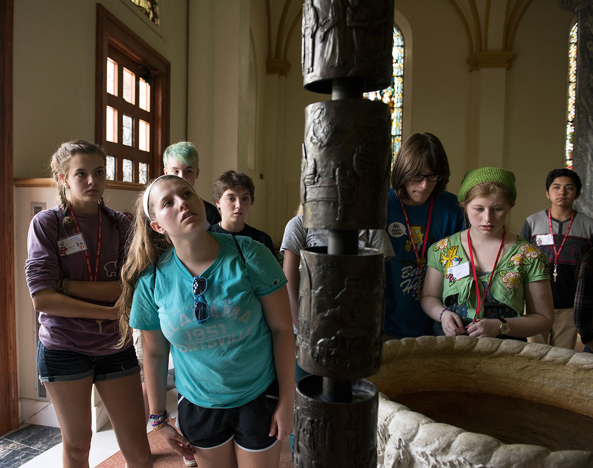 Rhiannon Hussung of Louisville examines the carvings on a candle stand at the entrance to the Archabbey Church at Saint Meinrad Archabbey in Saint Meinrad, Ind., while on a Humanities field trip Tuesday, July 5. (Photo by Tucker Allen Covey)