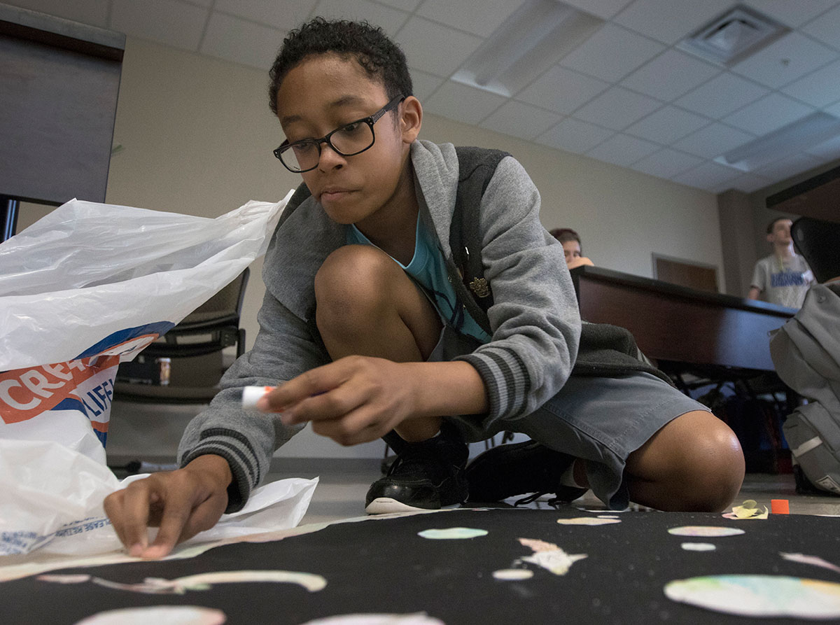 Karson Green of Bowling Green glues down pieces of his project in Einstein in Monet's Garden Thursday, June 22. Students splattered painted stars onto a black background before adding watercolor planets to create a space landscape. (Photo by Brook Joyner)
