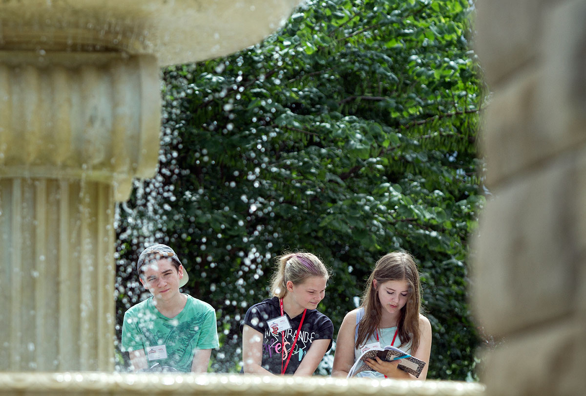 Lucas Nofsinger (from left) of Louisville, Audrey Thacker of Louisville, and Arden Ensor of Lexington write observations about the fountain in front of Van Meter Hall during a walk around campus with their Writing classmates Friday, June 30. (Photo by Sam Oldenburg)