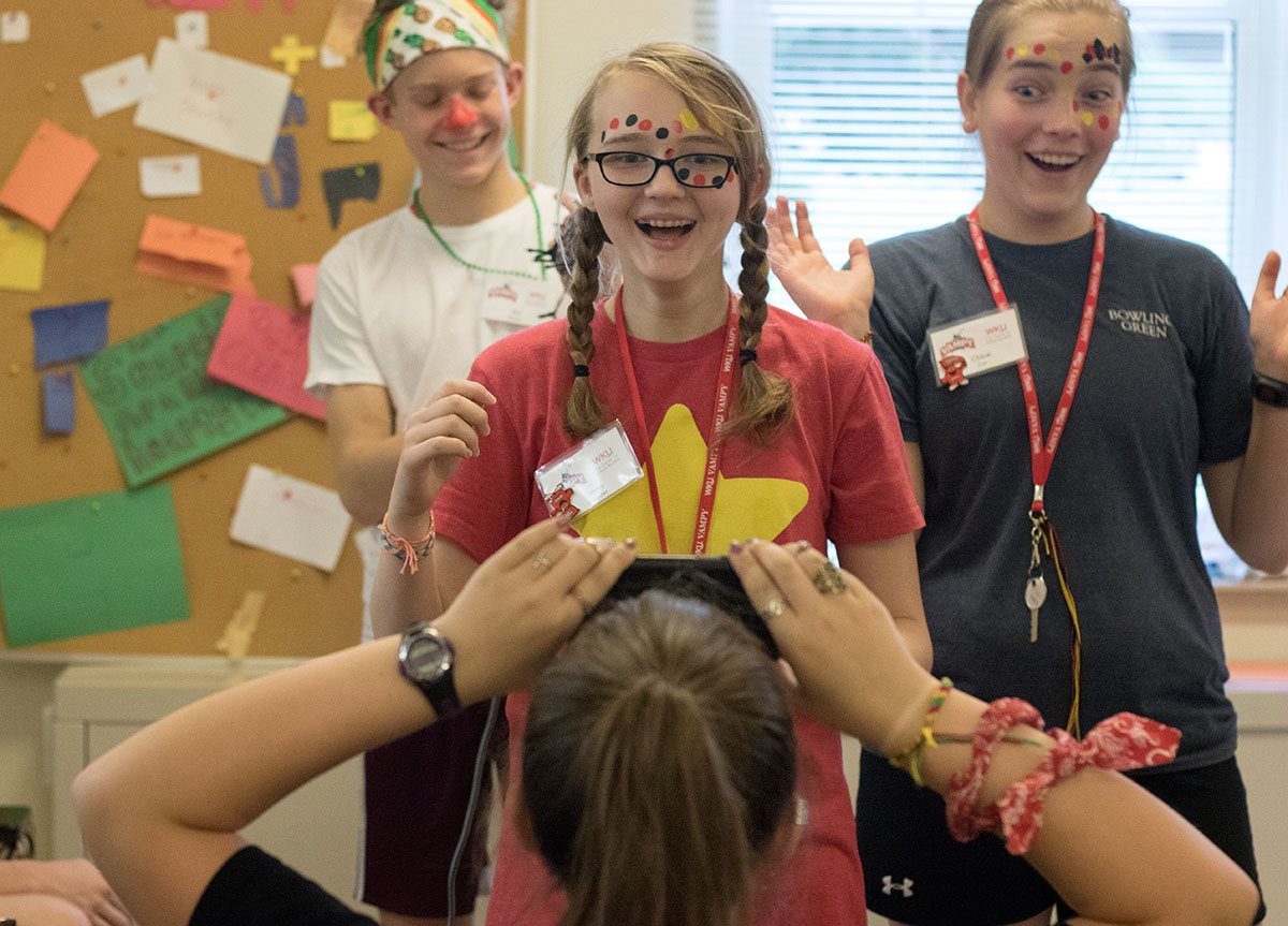 Emmy Rastoder (middle) of Bowling Green and Chloe Cox of Clarkson give clues to Arden Ensor of Lexington during a game of Heads Up at VAMPY Olympics July 1. Because of bad weather, campers had to compete in alternate events indoors. (Photo by Brook Joyner)