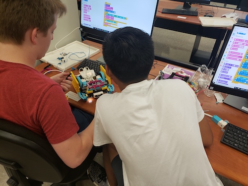 Two students work on a small robot in front of a computer..
